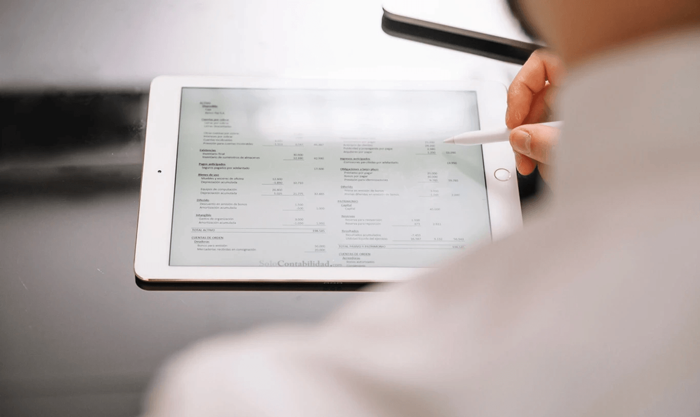 Person som använder en penna på en surfplatta som visar ett finansiellt dokument med tabeller och figurer.